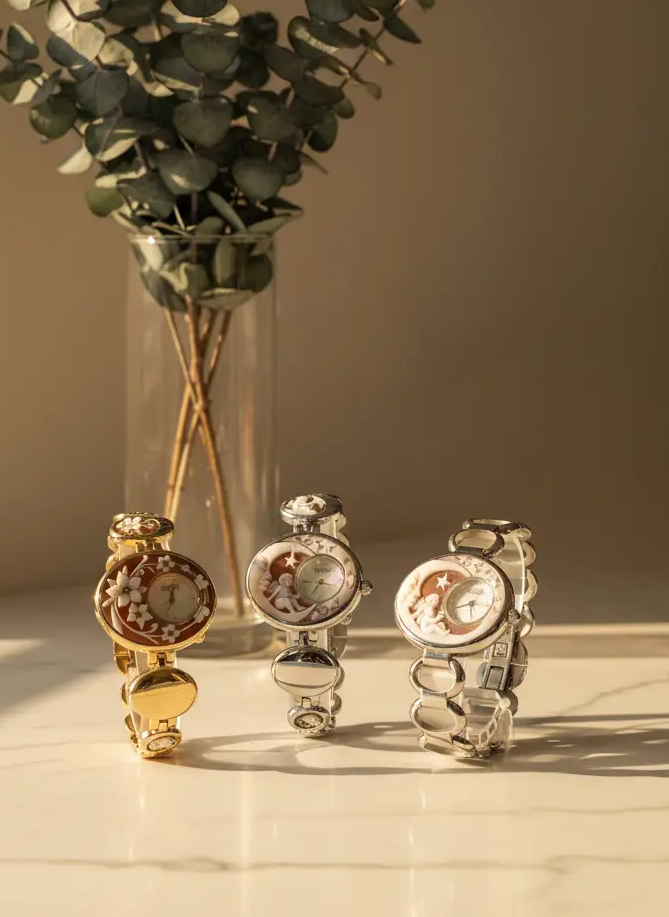 Three decorative watches on a marble surface with a vase of greenery in the background.