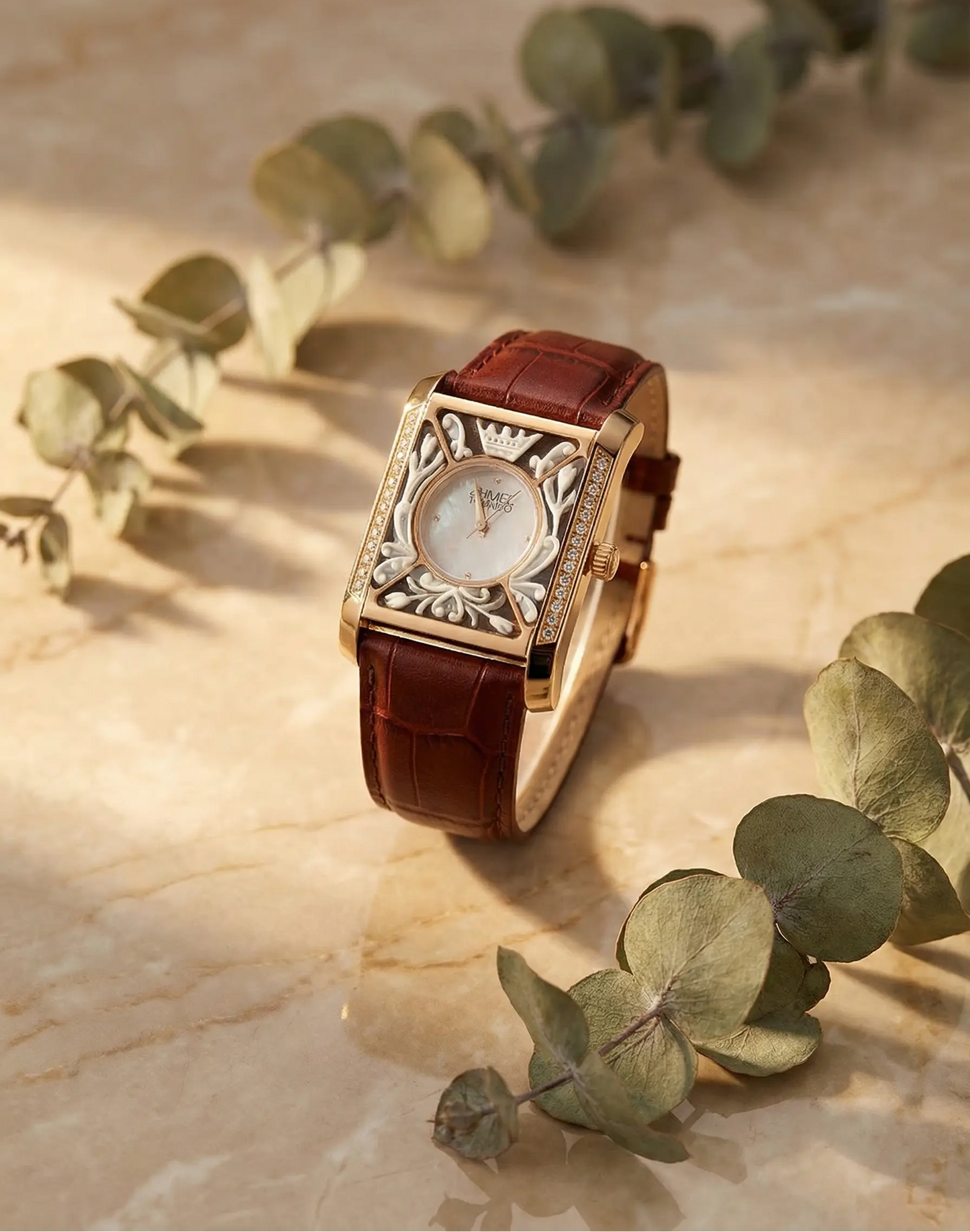 Luxury old money watch with brown leather strap on a beige surface with eucalyptus leaves
