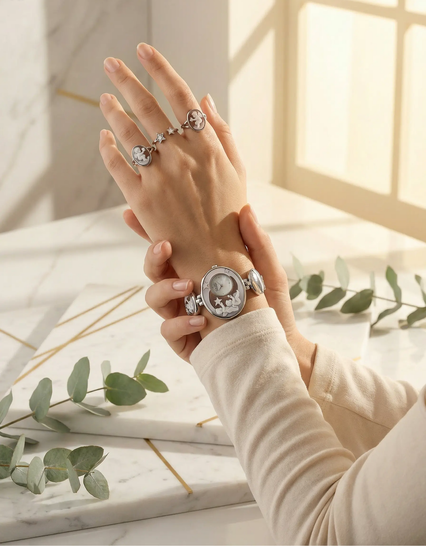 Hand wearing a silver watch with floral design on a marble surface with greenery