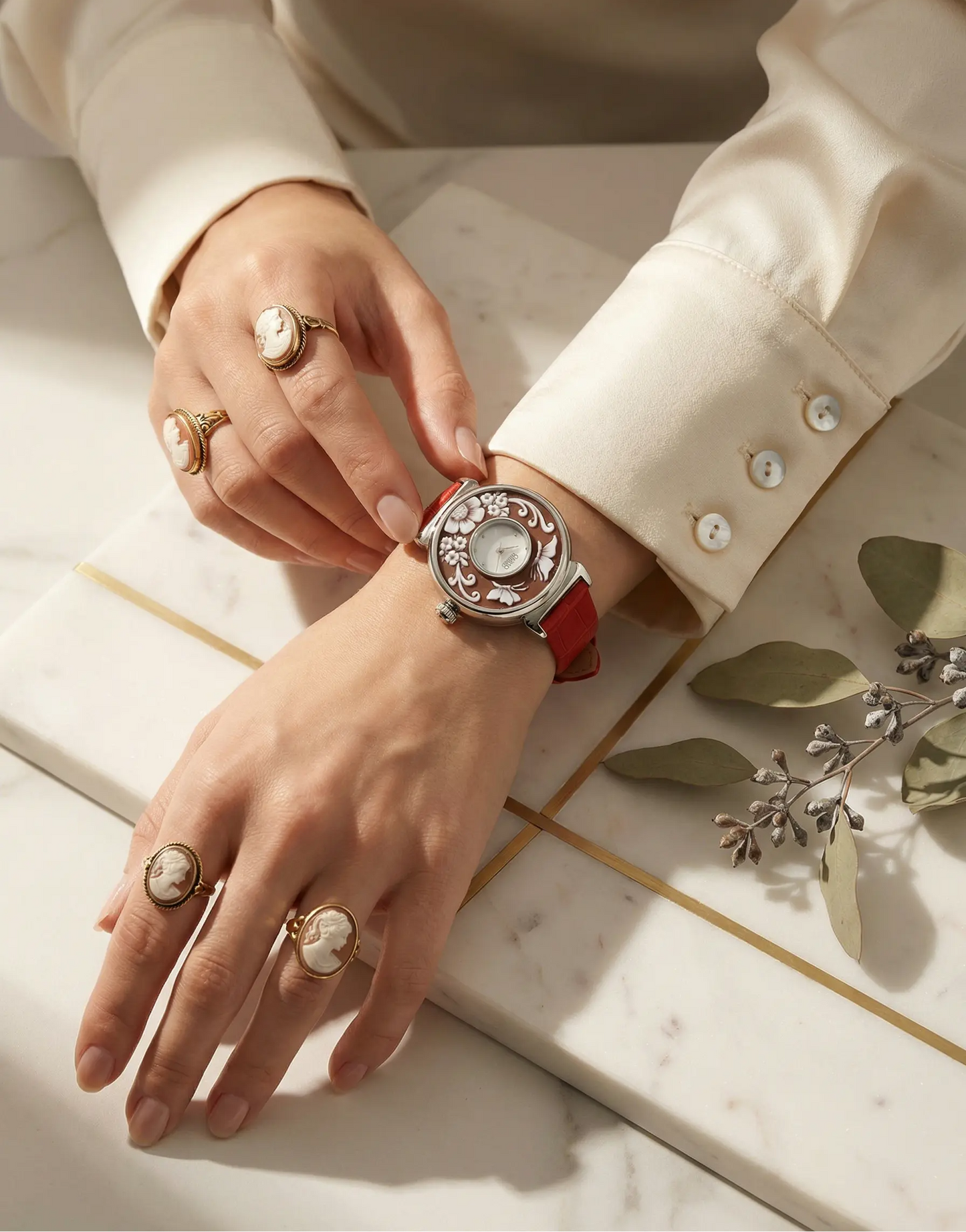 Close-up of a hand wearing a red watch with intricate design on a marble surface.
