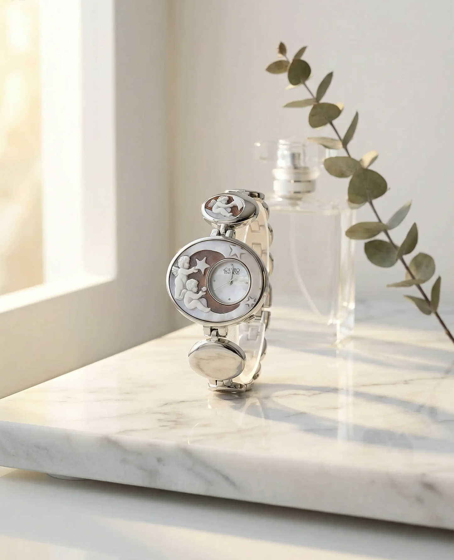 Silver watch with moon and star design on a marble surface with a bottle and plant in the background