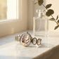 Silver bracelet with intricate design on a marble surface next to a clear glass bottle.