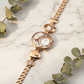 Rose gold bracelet with heart-shaped links on a marble surface with eucalyptus leaves