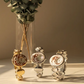 Three decorative watches on a marble surface with a vase of greenery in the background.