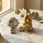 Decorative watch and gold monkey figurine on a marble surface with leaves in the background