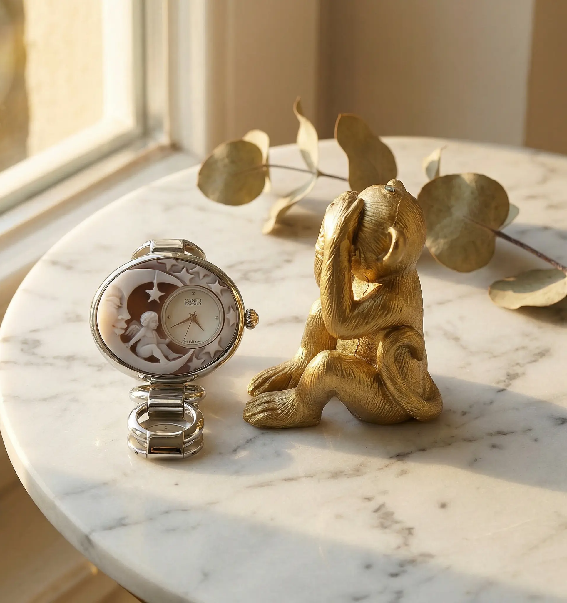 Decorative watch and gold monkey figurine on a marble surface with leaves in the background