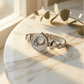 Silver watch with decorative face on a marble surface with eucalyptus leaves