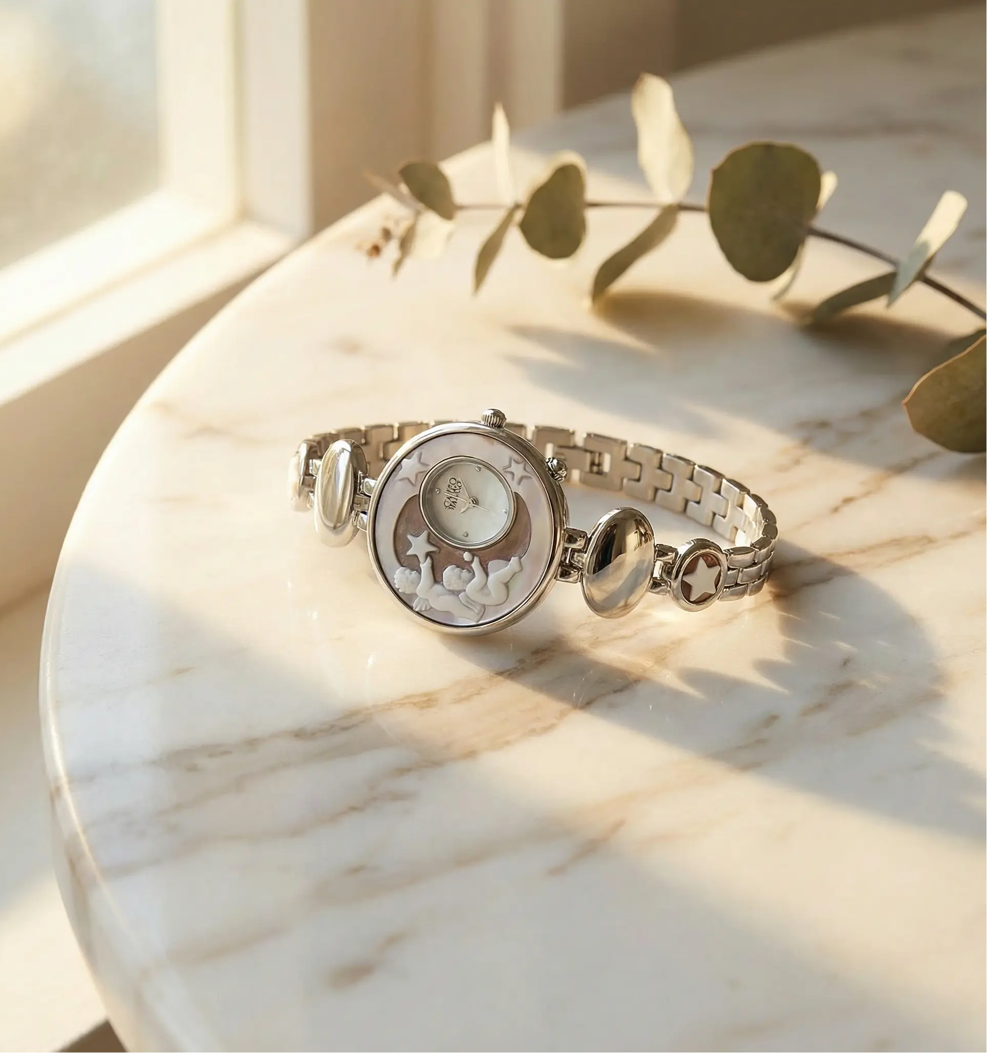 Silver watch with decorative face on a marble surface with eucalyptus leaves