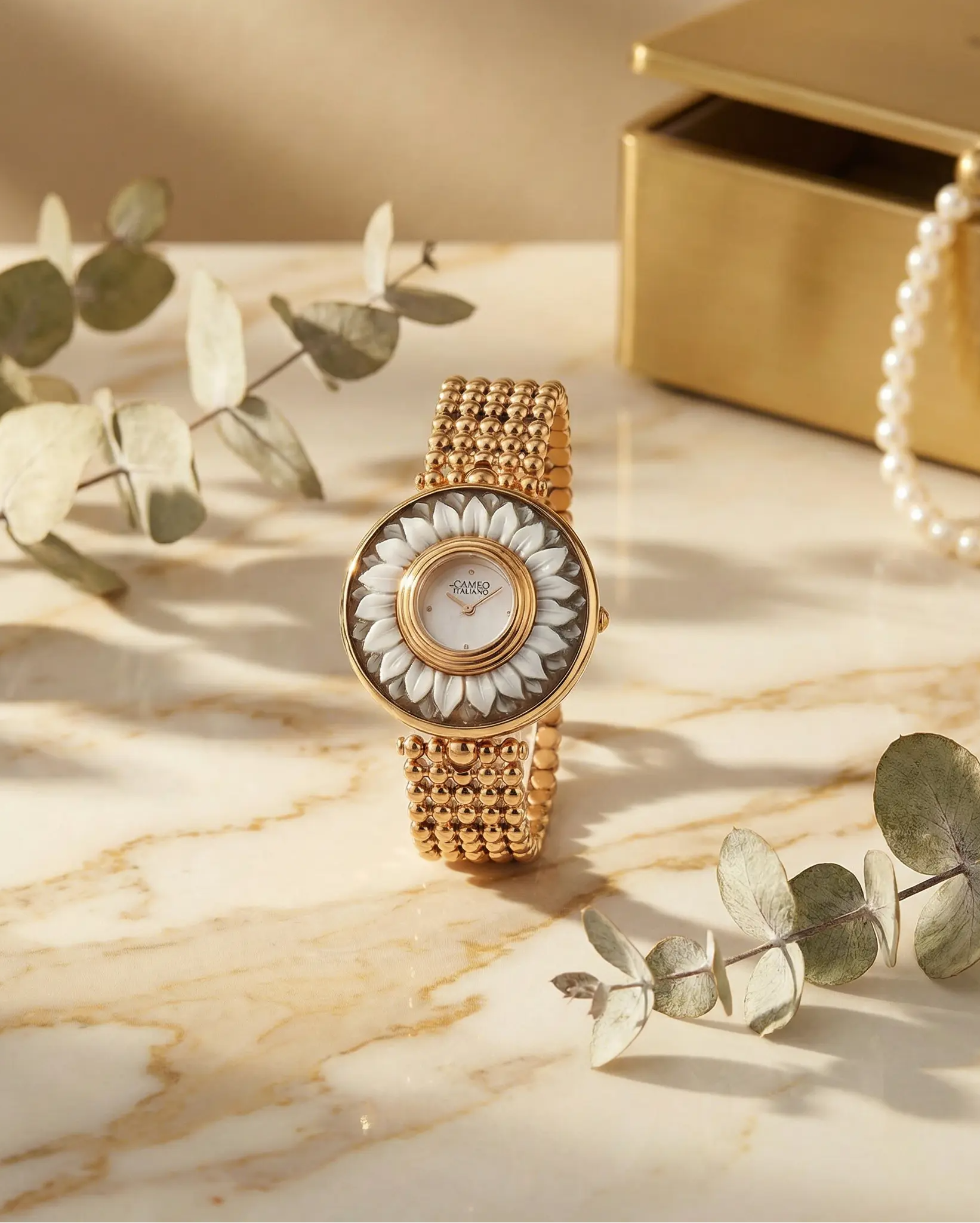 old money Gold watch with floral design on a marble surface with green leaves and a gold box.