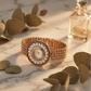Gold watch with floral face on marble surface with leaves and perfume bottle