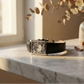 Black leather belt with silver buckle on a marble surface near a vase with dried flowers.