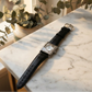cameo Watch with a black leather strap on a marble surface with greenery in the background
