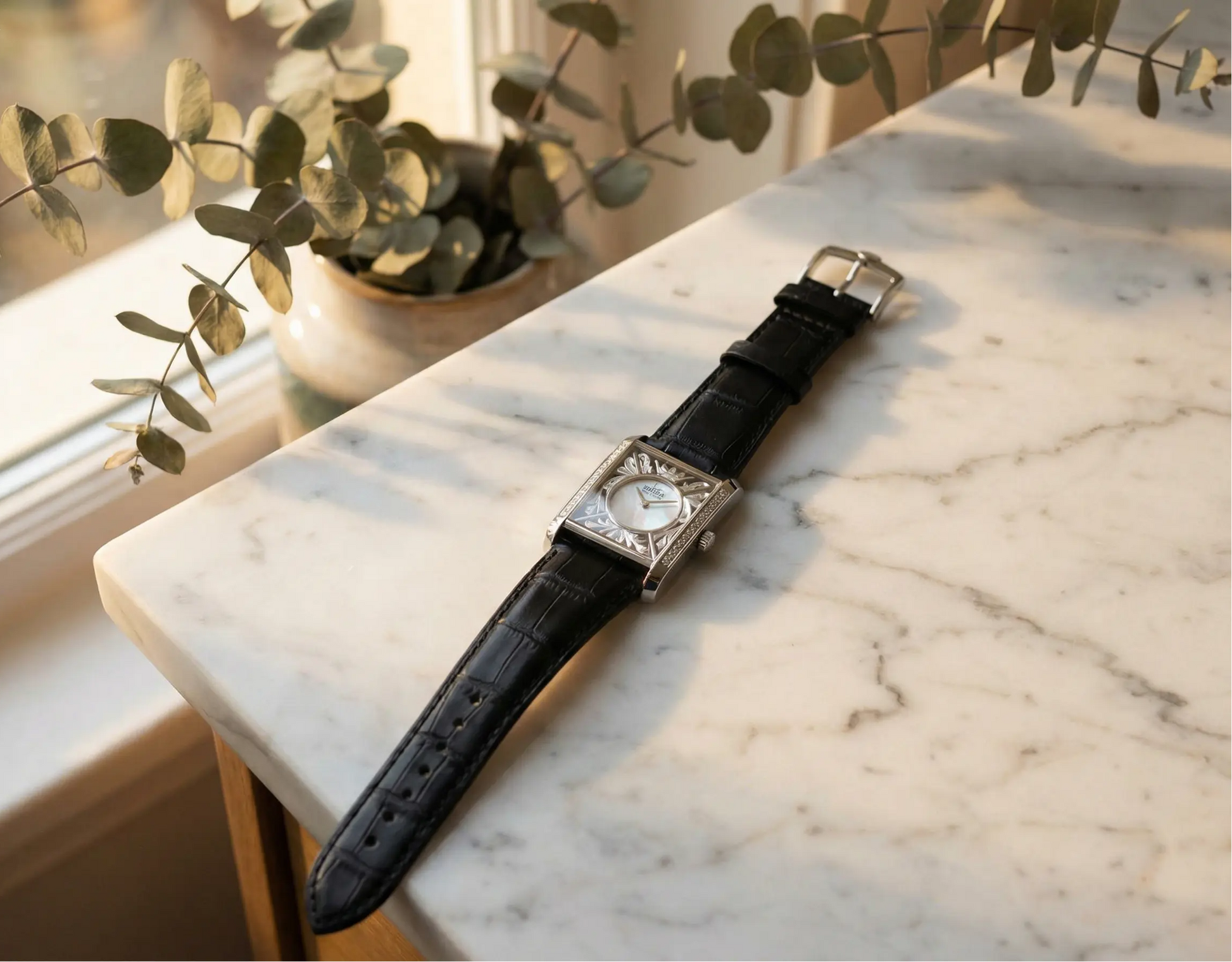 cameo Watch with a black leather strap on a marble surface with greenery in the background