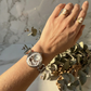 Hand wearing a silver watch with visible brand logo, against a marble wall background.