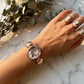 Hand wearing a bracelet and rings on a marble surface with greenery
