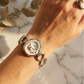 Hand wearing a silver bracelet with a circular design on a marble surface with eucalyptus leaves in the background.