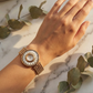 Gold floral watch on a wrist with a marble background and green leaves