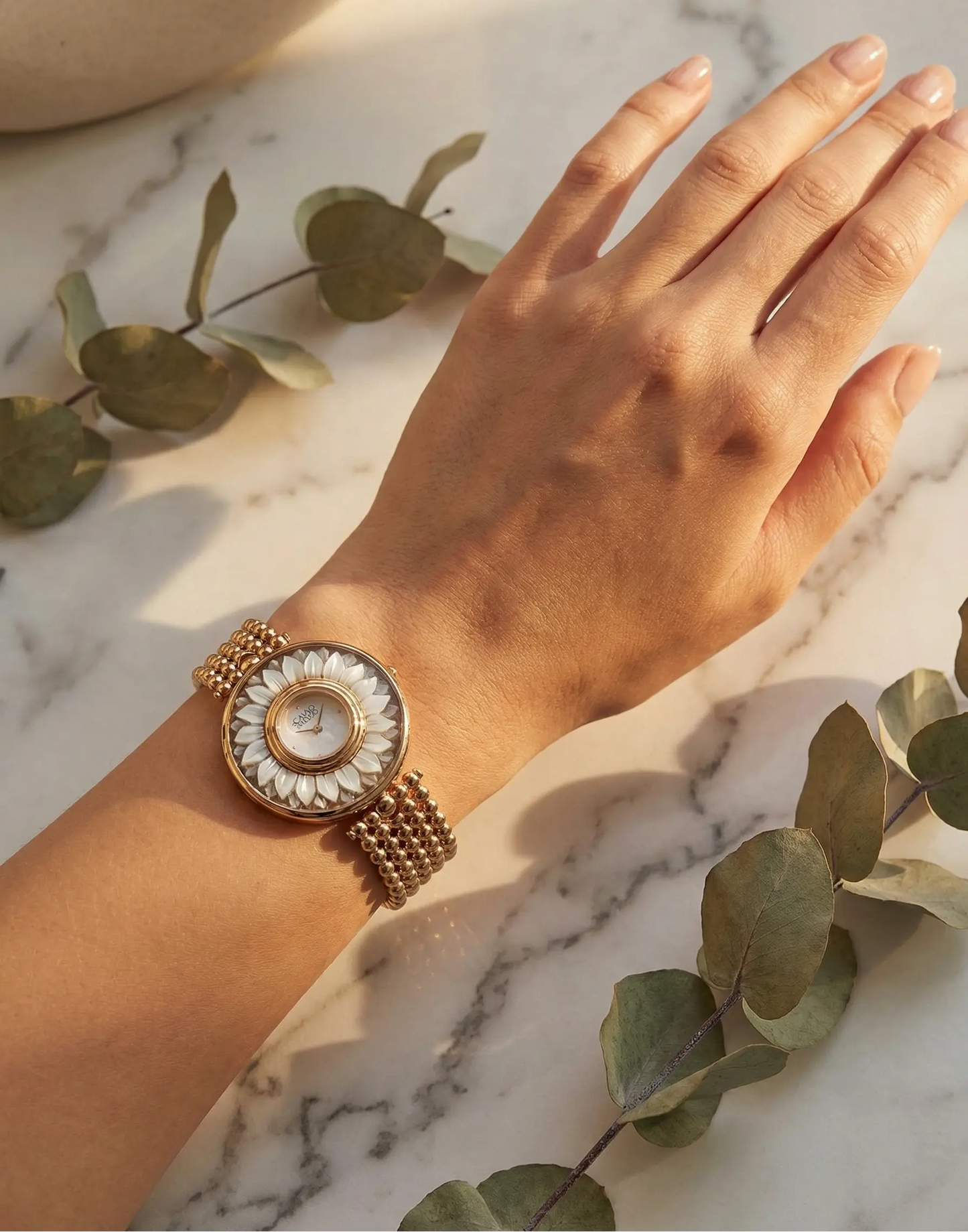 Gold floral watch on a wrist with a marble background and green leaves