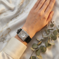 Hand wearing an antique watch on a marble surface with green leaves.
